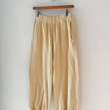 Yellow pants hanging on a wooden hanger against a white wall