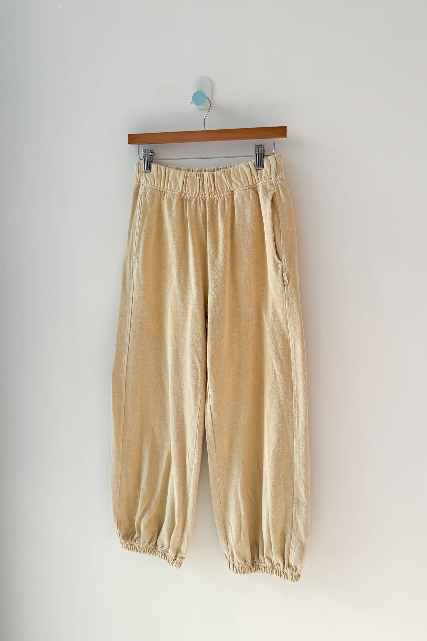 Yellow pants hanging on a wooden hanger against a white wall