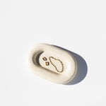 white stone catch all tray holding earrings and a bracelet, white background