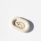 white stone catch all tray holding earrings and a bracelet, white background