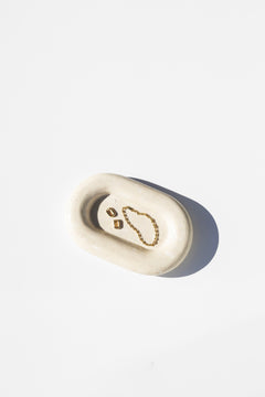 white stone catch all tray holding earrings and a bracelet, white background