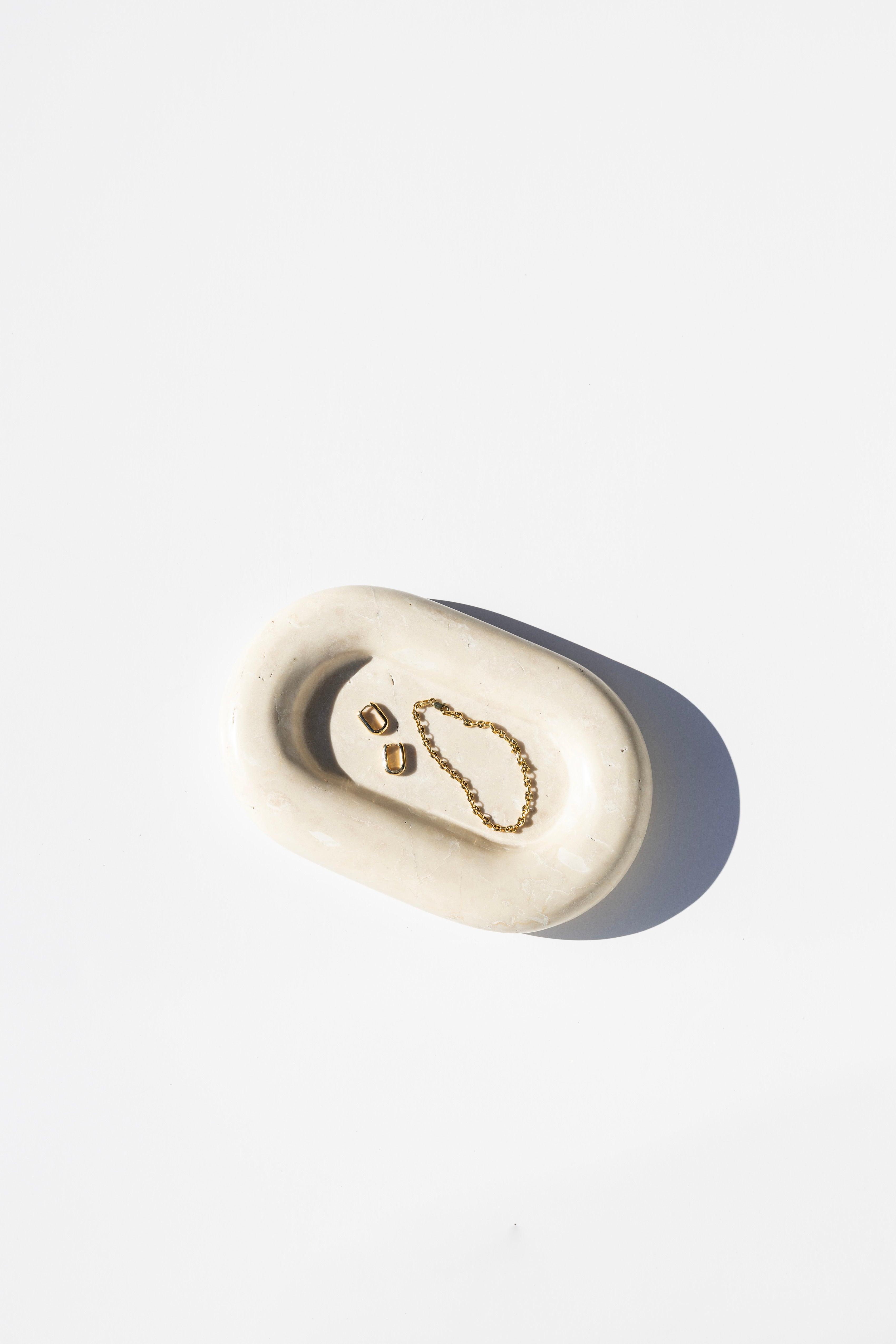 white stone catch all tray holding earrings and a bracelet, white background