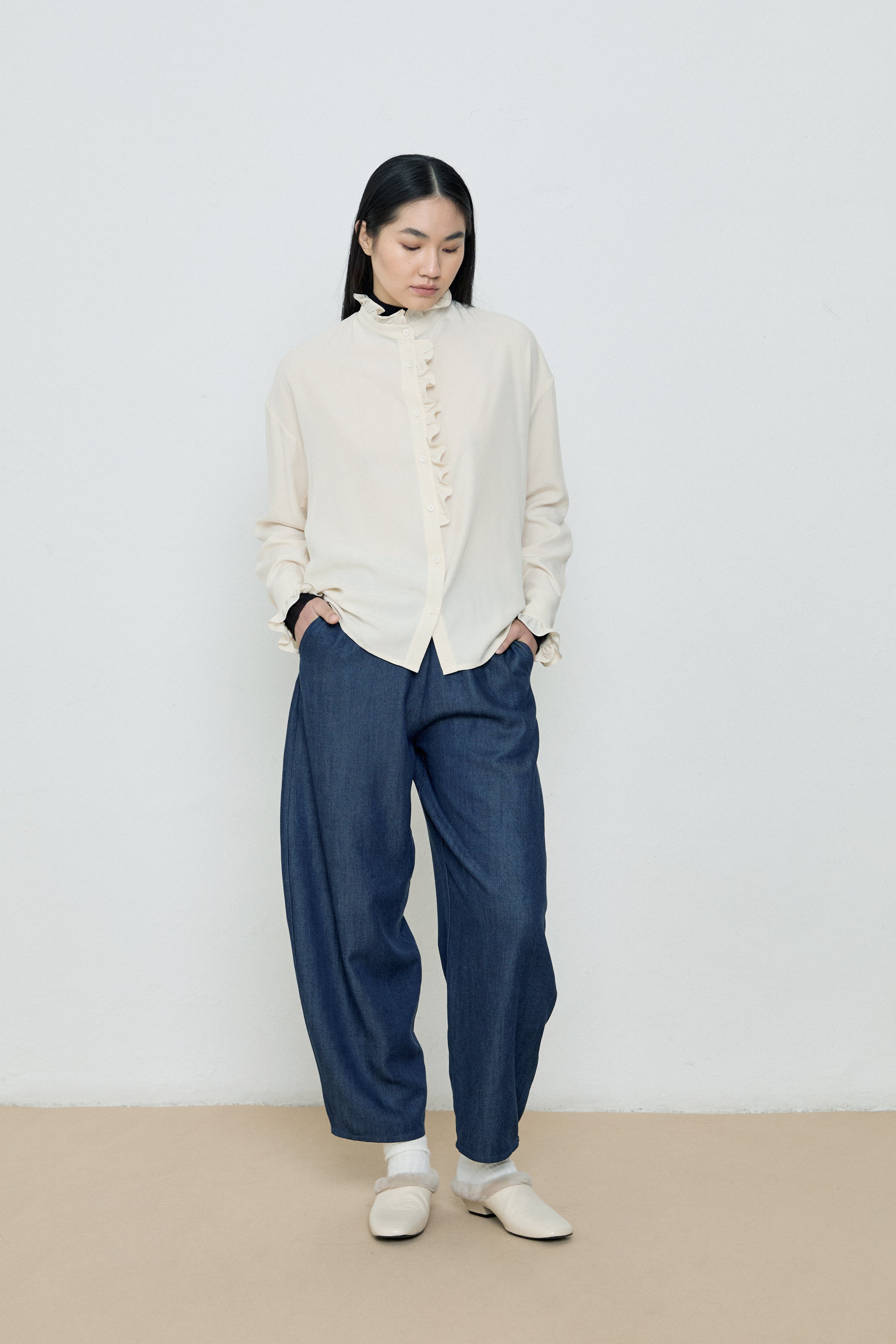 Person wearing a white blouse and blue pants against a plain background