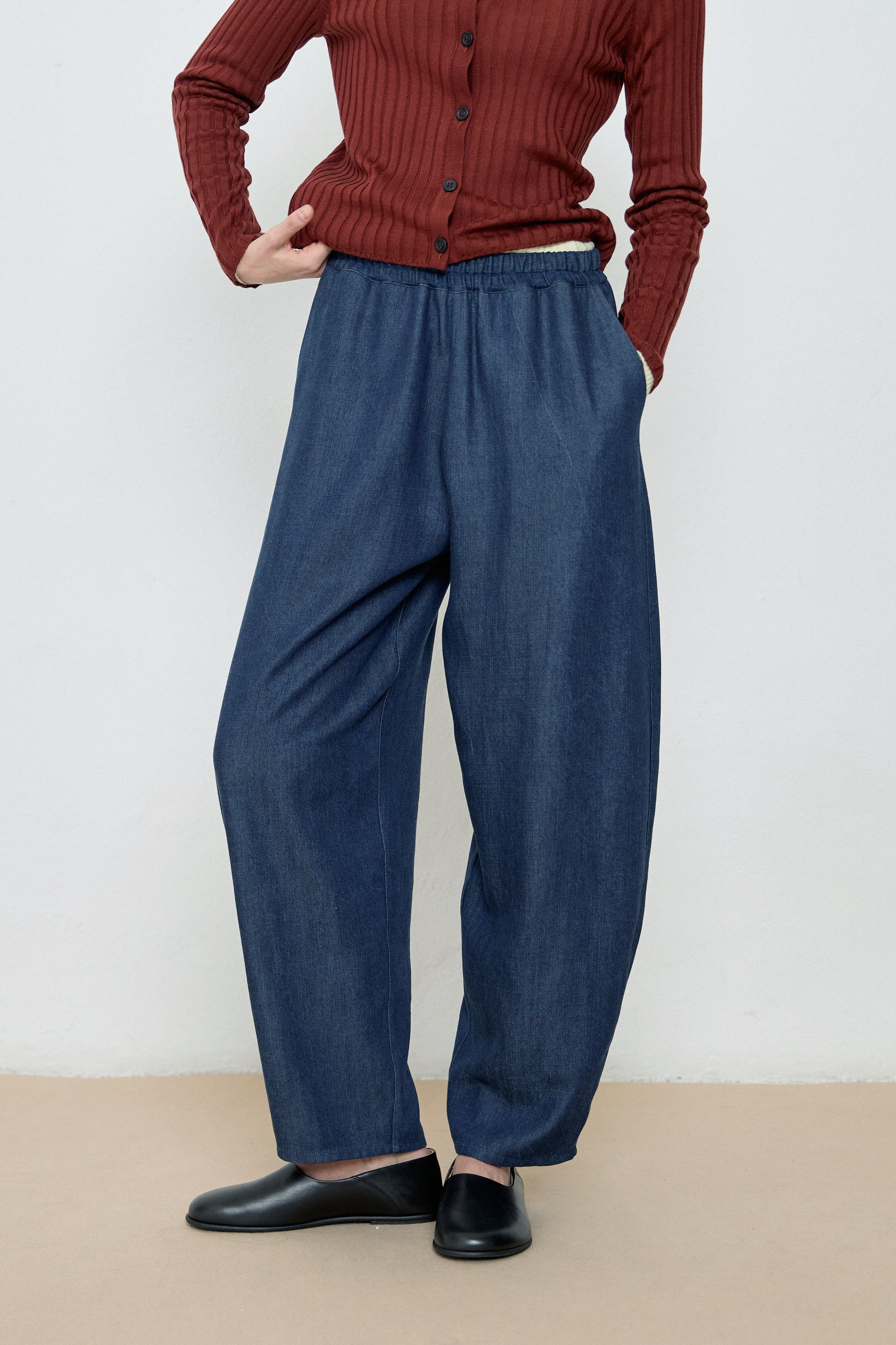 Person wearing a red ribbed sweater and blue wide-leg pants on a plain background