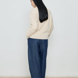 Person wearing a beige sweater and blue pants against a white background