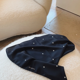 Black satin scarf with white polka dots on a white cushion next to a beige armchair.