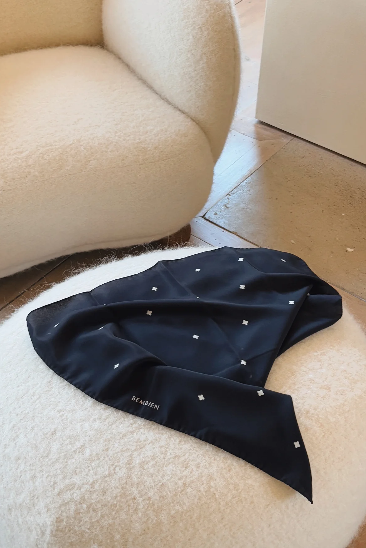 Black satin scarf with white polka dots on a white cushion next to a beige armchair.