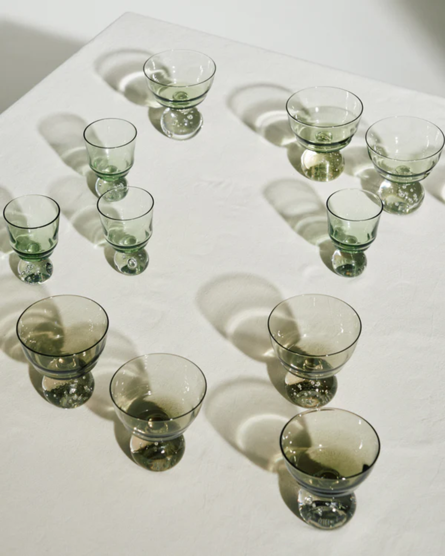Green glass tumblers arranged on a white surface with shadows.