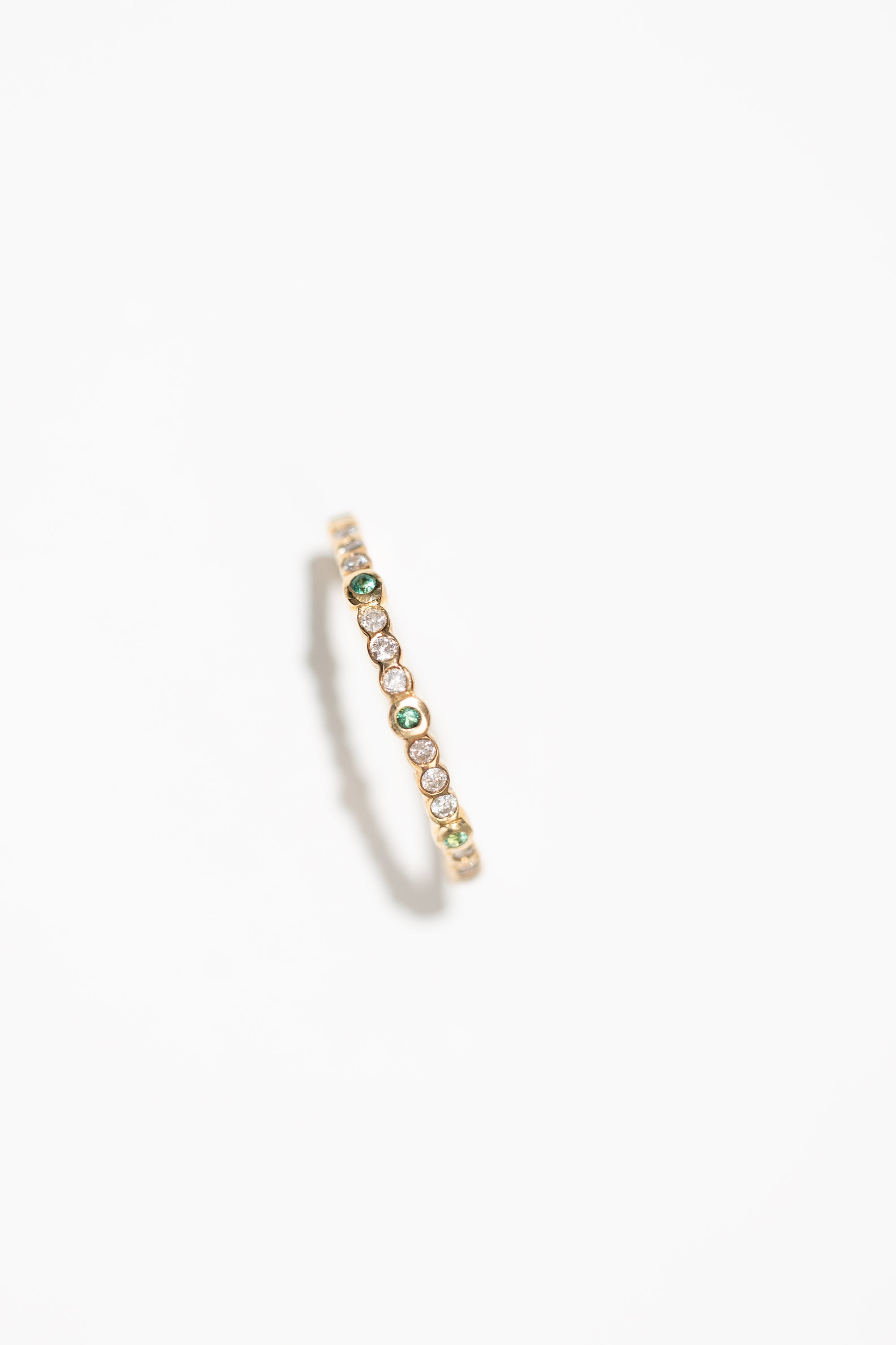 A gold stacking ring with bezel set diamonds and emeralds, on a white background.