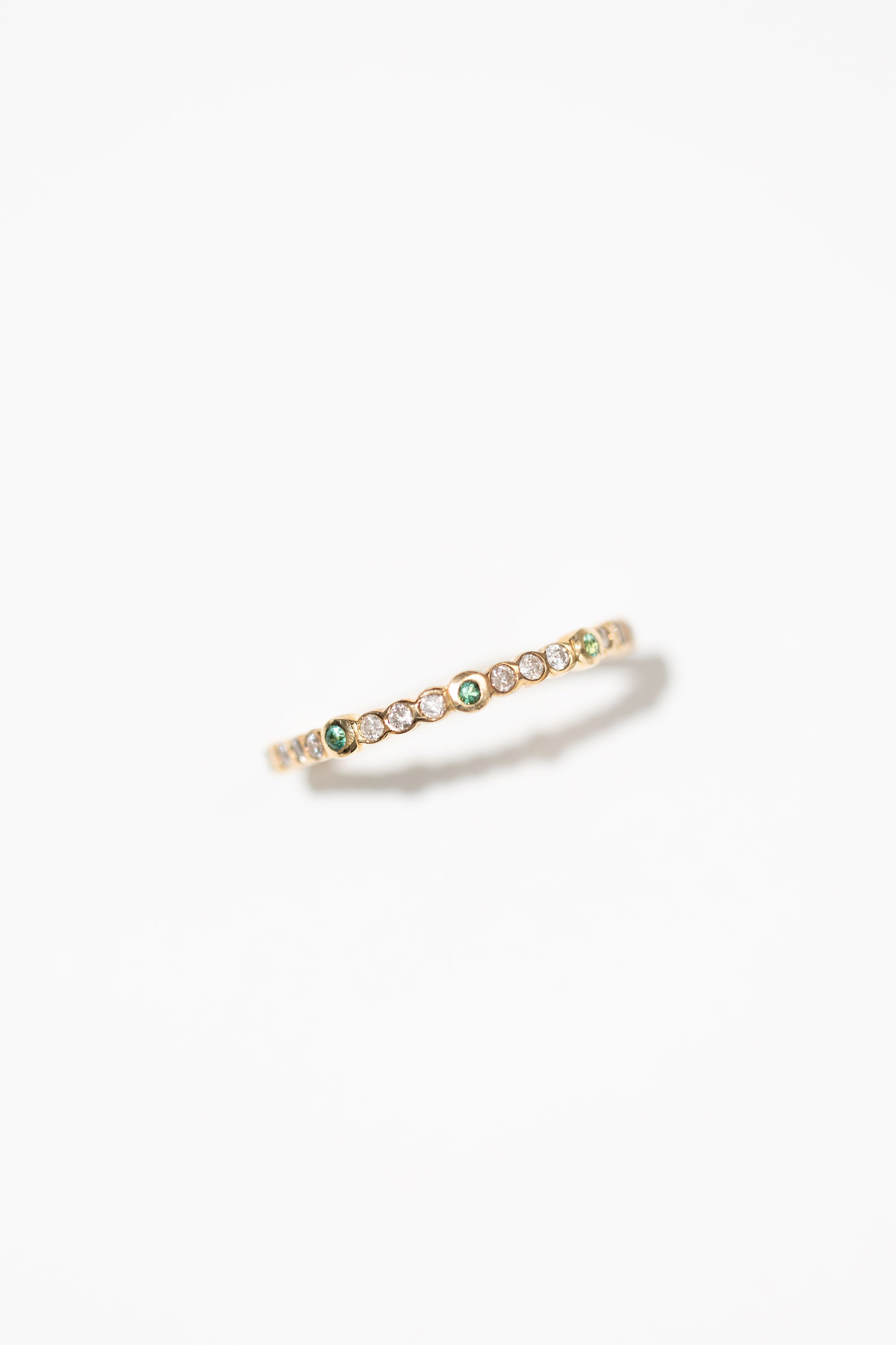 A gold stacking ring with bezel set diamonds and emeralds, on a white background.