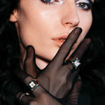 Woman wearing black gloves and a ring with a diamond against a dark background