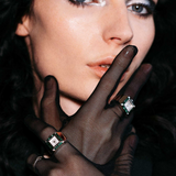 Woman wearing black gloves and a ring with a diamond against a dark background