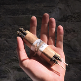 Hand holding two lit cigarettes against a dark stone wall background
