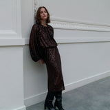Woman in a brown sequin dress standing against a white wall.