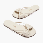 Pair of cream-colored sandals with bow details on a white background