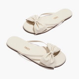 Pair of cream-colored sandals with bow details on a white background