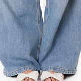 White sandals with bow details worn with blue jeans on a white background