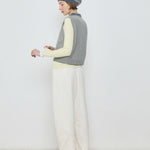 Person wearing a striped sweater vest, white pants, and a beanie against a plain background