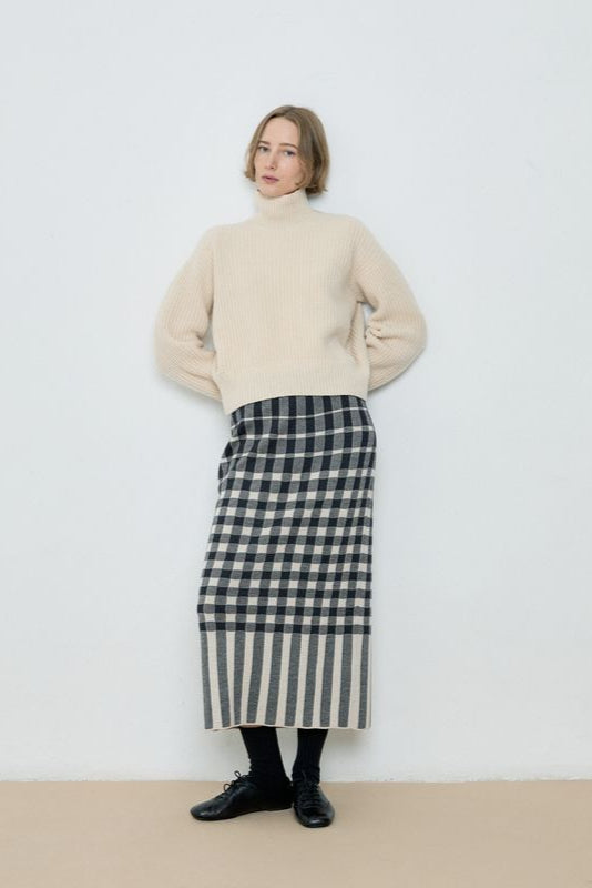 Woman wearing a beige sweater and black and white checkered skirt against a plain background