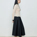 Woman wearing a beige sweater and black skirt against a white background