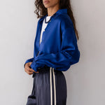 Woman wearing a blue silk shirt and dark pants with white stripes against a plain background