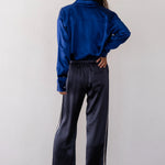 Person wearing a blue satin shirt and dark pants with white stripes against a plain background