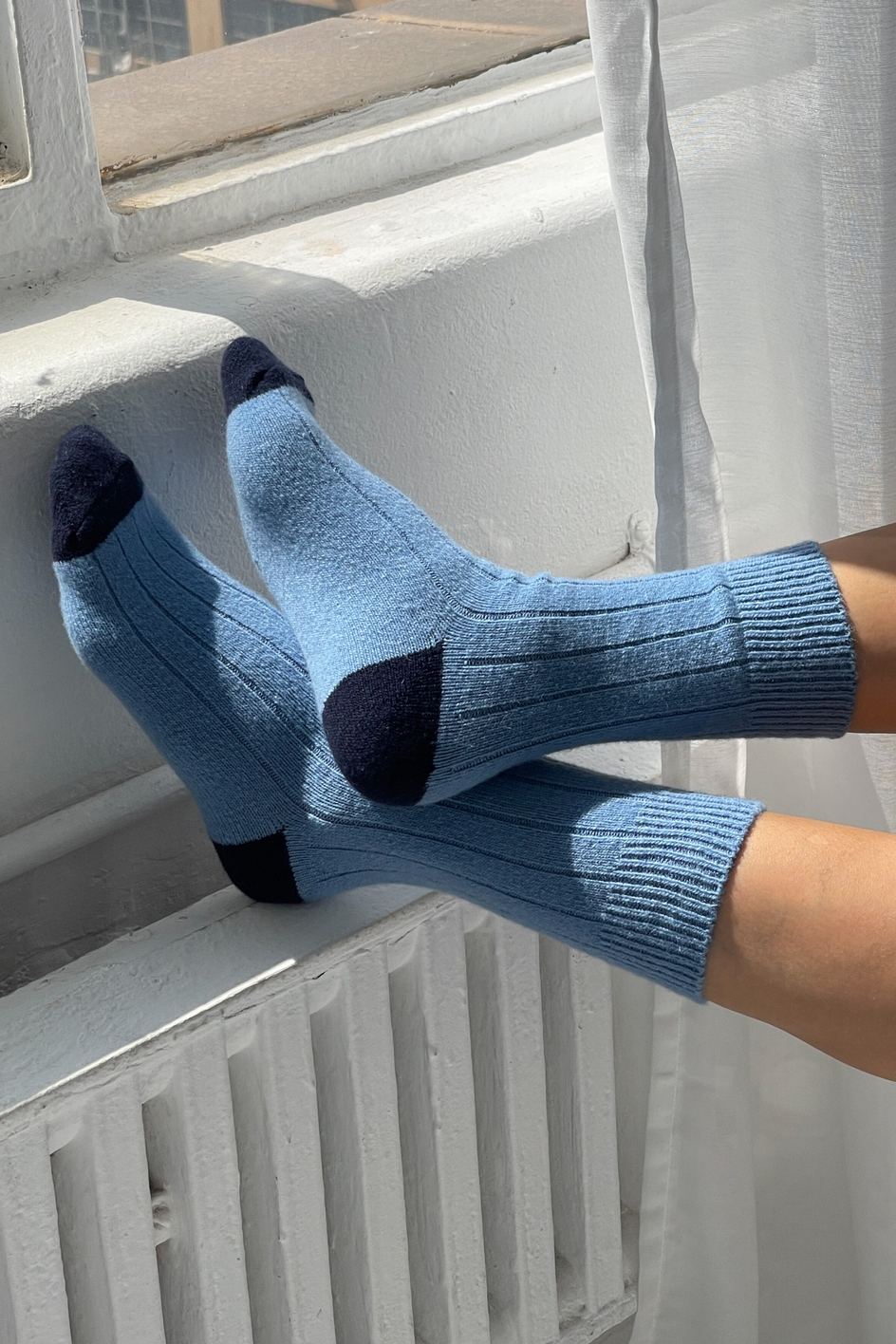 Blue socks with black toes and cuffs worn by a person sitting on a radiator.