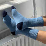 Blue socks with black toes and cuffs worn by a person sitting on a radiator.