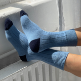 Blue socks with black toes and cuffs worn by a person sitting on a radiator.