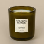 A green glass candle with a white label that reads 'CAROLINE FRANCIS' and 'Somewhere Late Summer'.