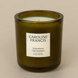A green glass candle with a white label that reads 'CAROLINE FRANCIS' and 'Somewhere Late Summer'.