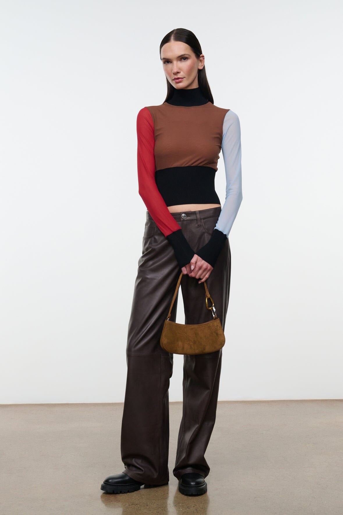 Model wearing brown leather trousers and holding the STAUD Ollie Bag in Cigar suede