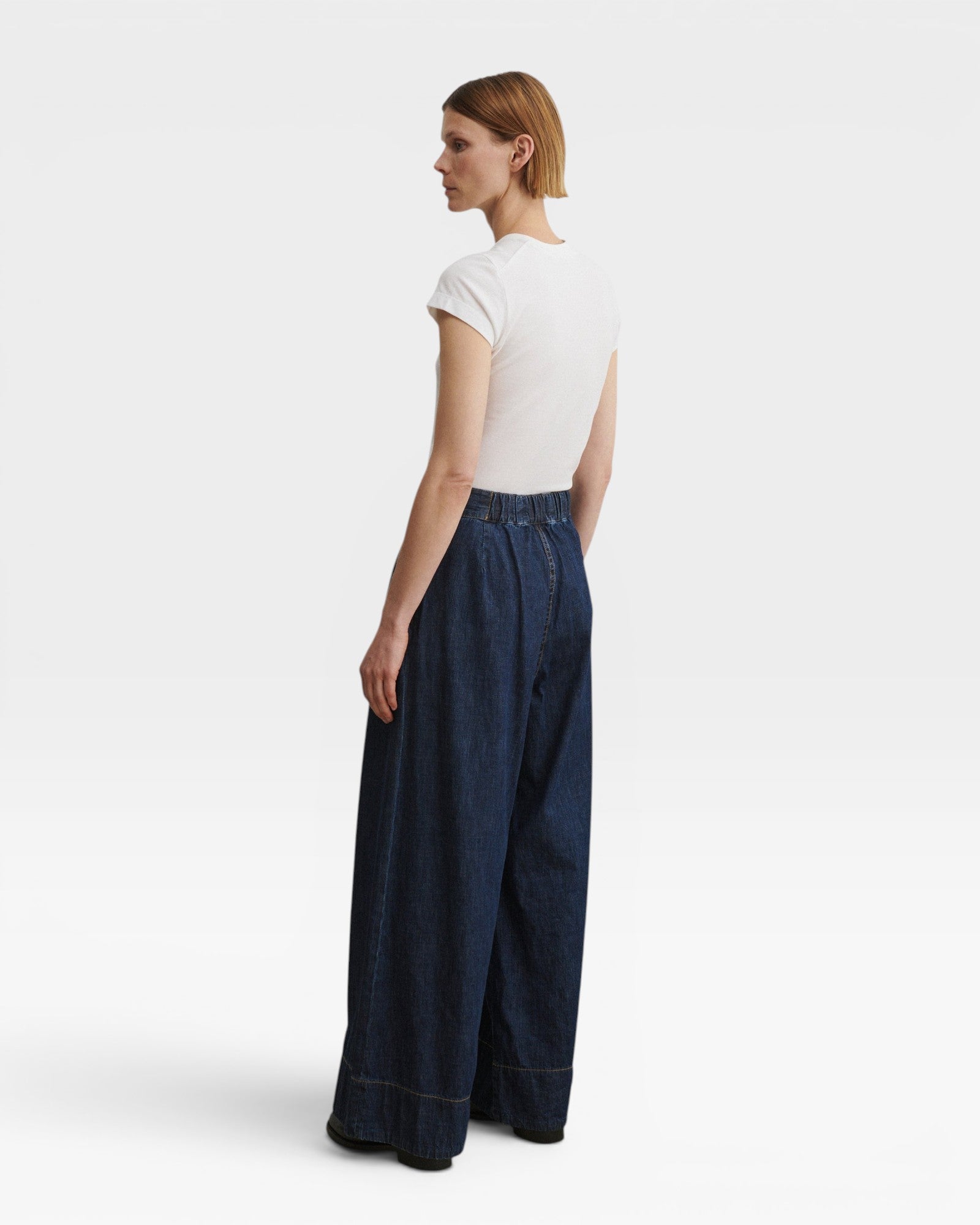 JONES + CO Coxsone dark indigo denim trousers, back three-quarter view with elastic back waistband.