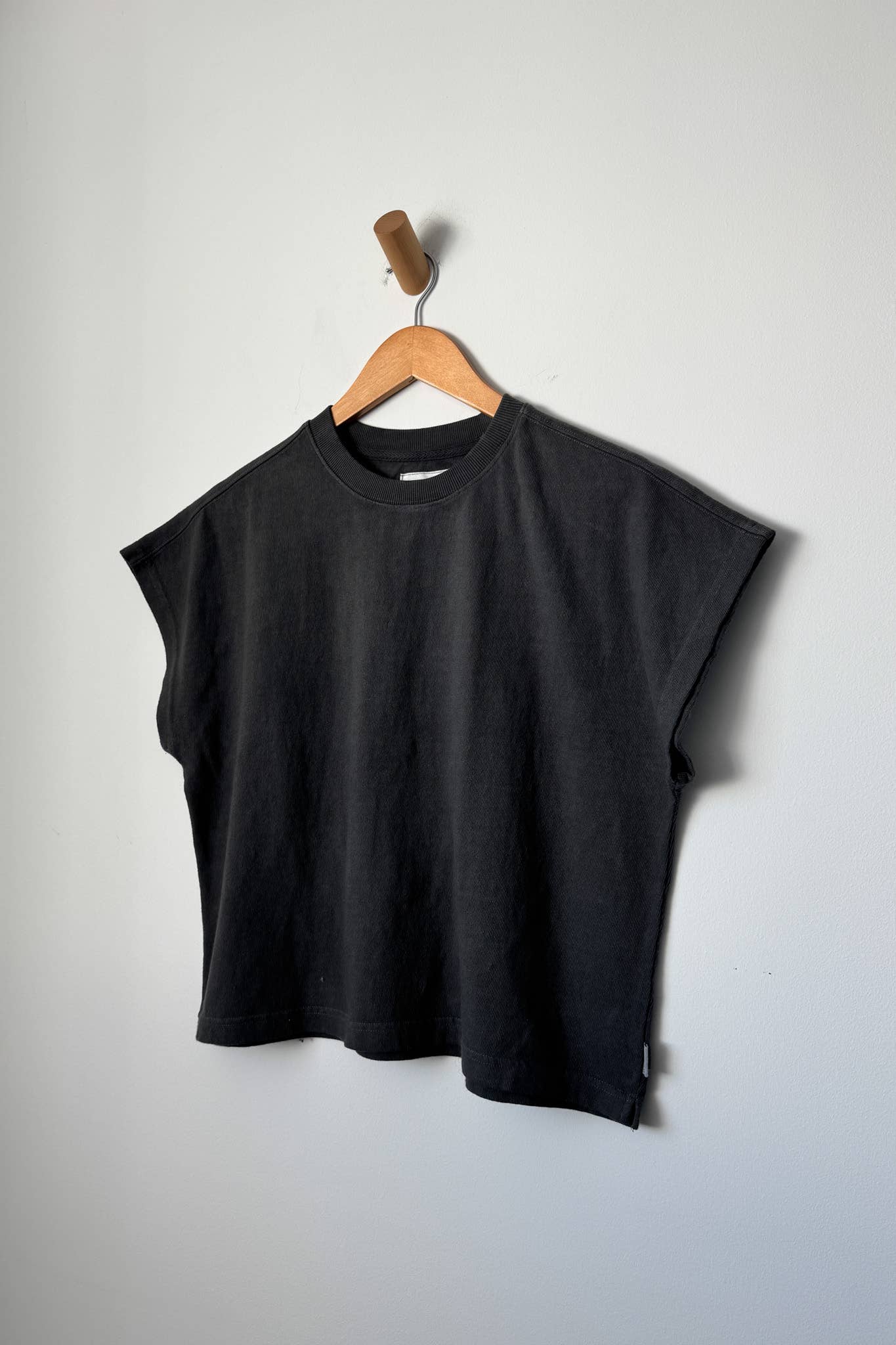 Black sleeveless top on a wooden hanger against a plain background