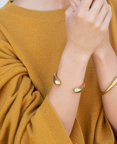 Person wearing a gold bracelet on a mustard yellow sweater