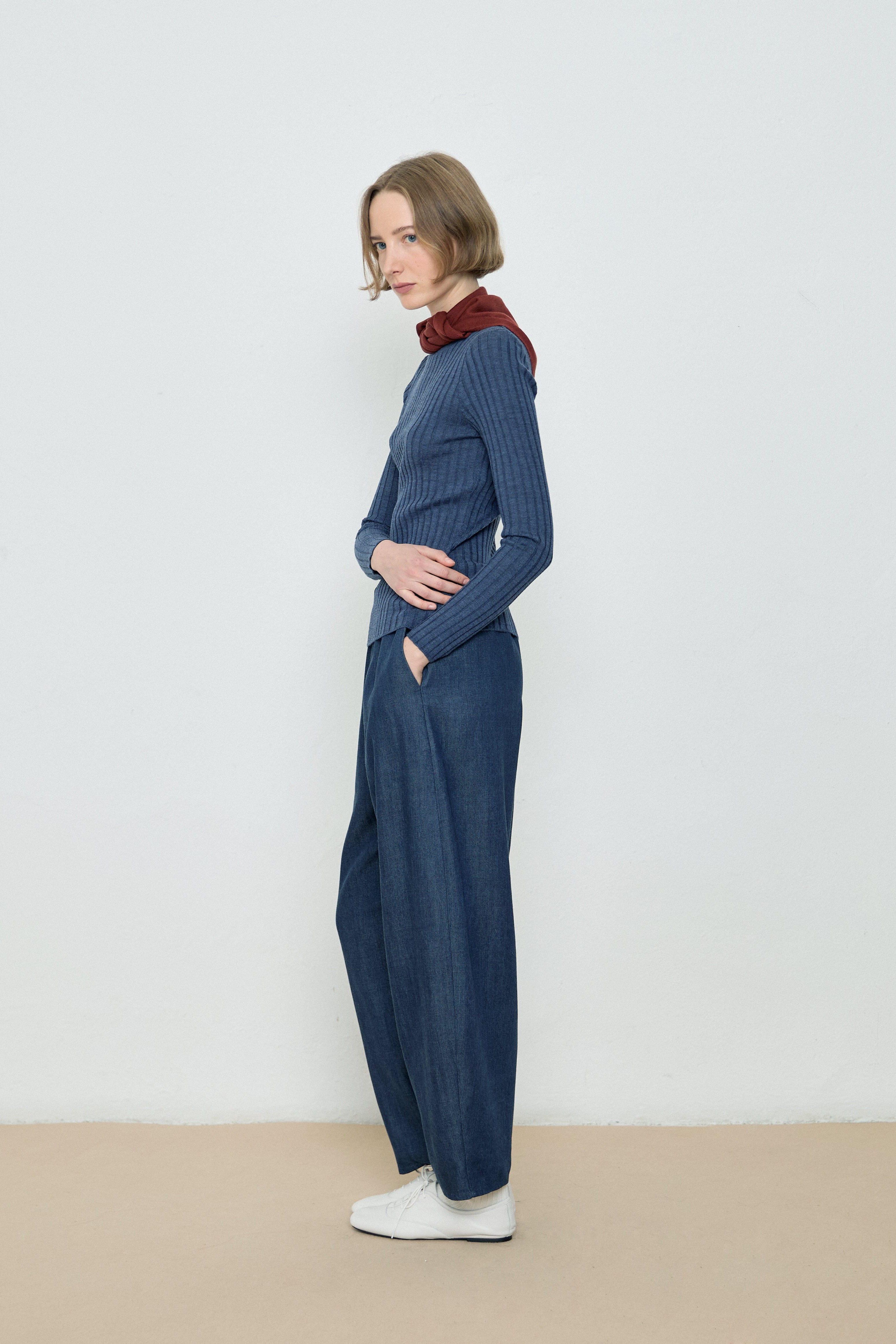 Woman wearing a blue ribbed sweater and dark blue wide-leg pants against a white background