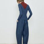 Person wearing a blue ribbed sweater and matching pants with a red hood, standing against a white wall.