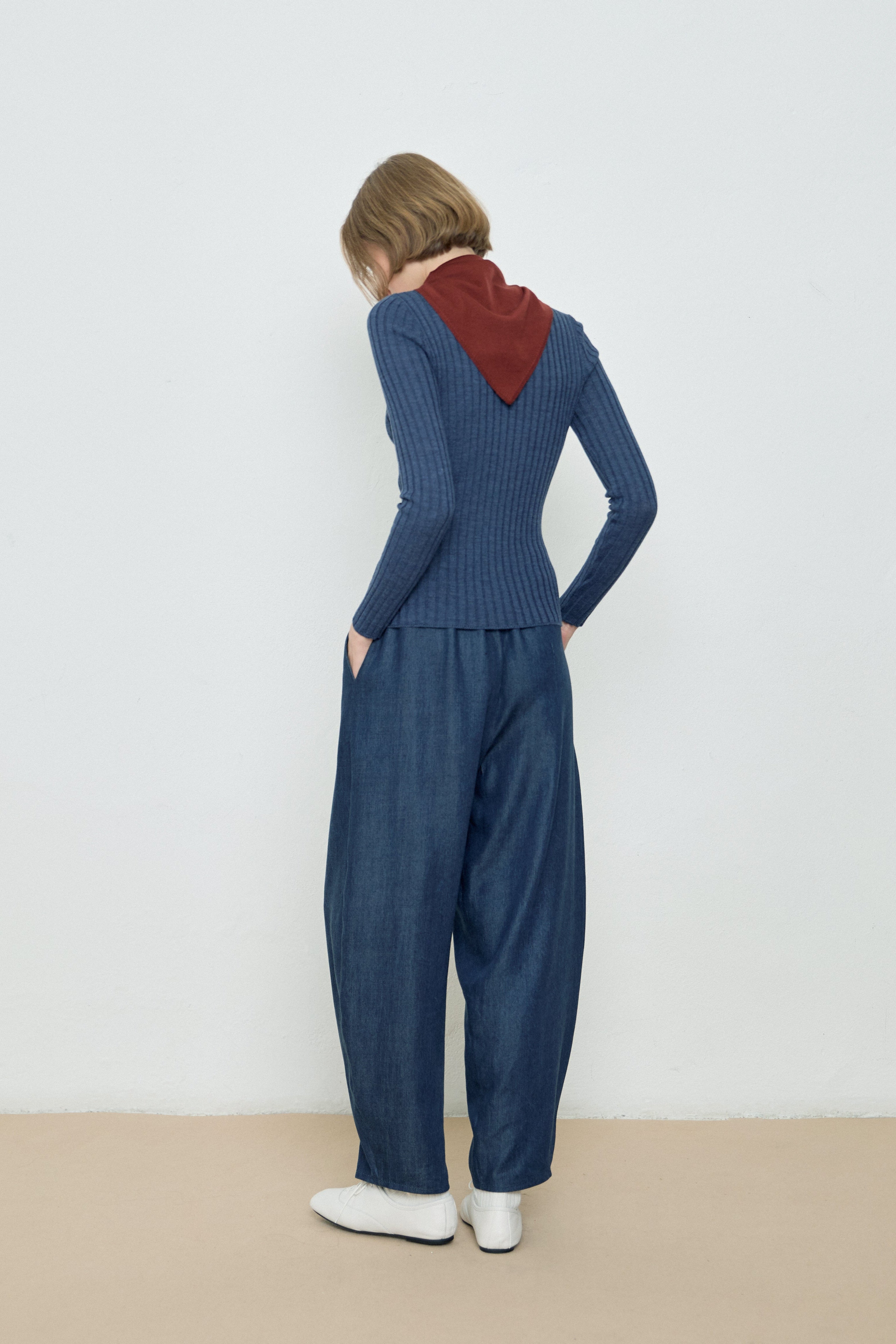 Person wearing a blue ribbed sweater and matching pants with a red hood, standing against a white wall.