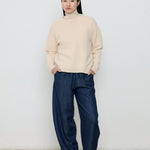 Person wearing a beige sweater and navy pants against a white background