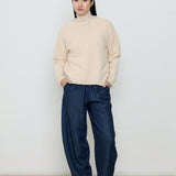 Person wearing a beige sweater and navy pants against a white background
