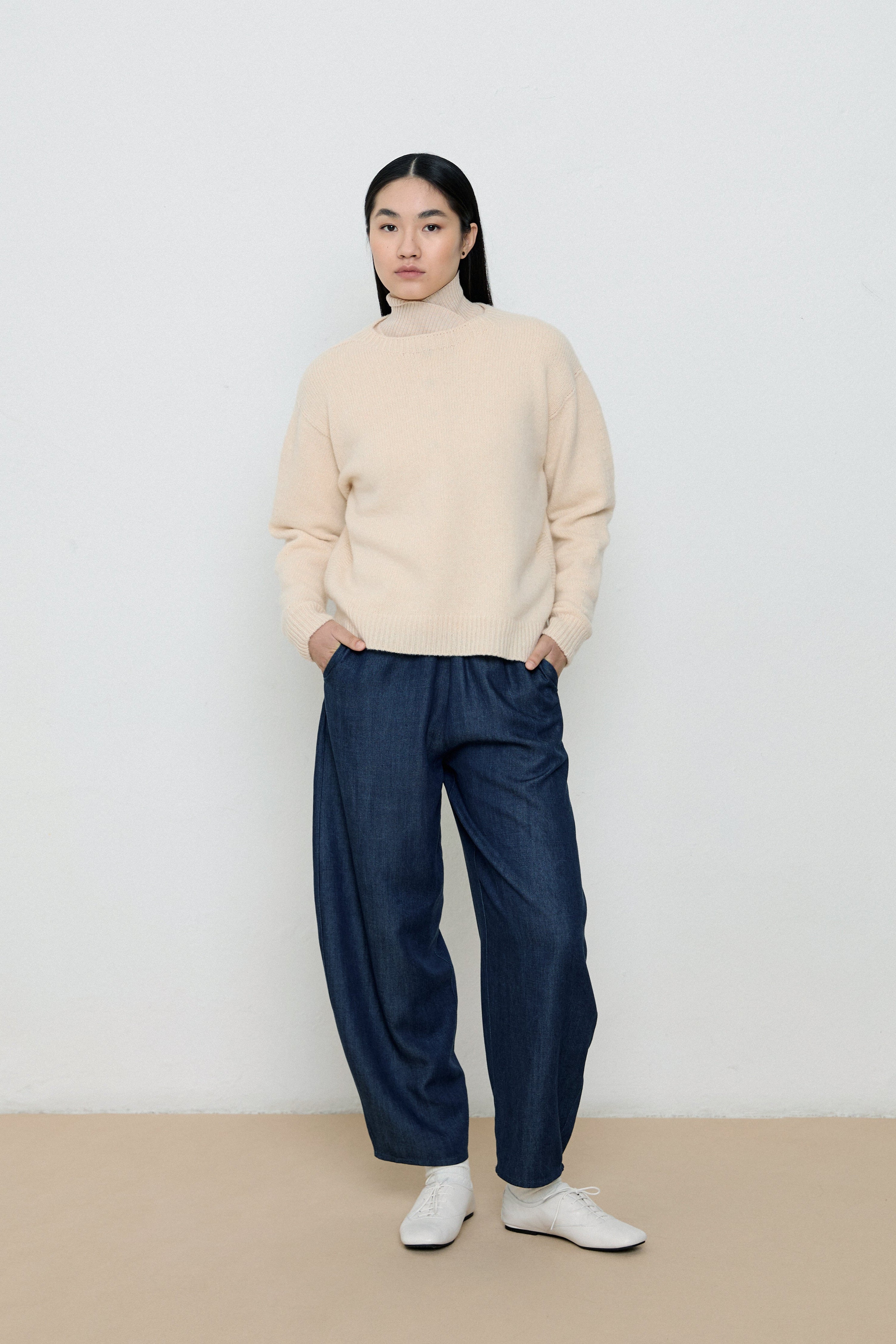 Person wearing a beige sweater and navy pants against a white background
