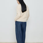 Person wearing a beige sweater and blue pants against a white background