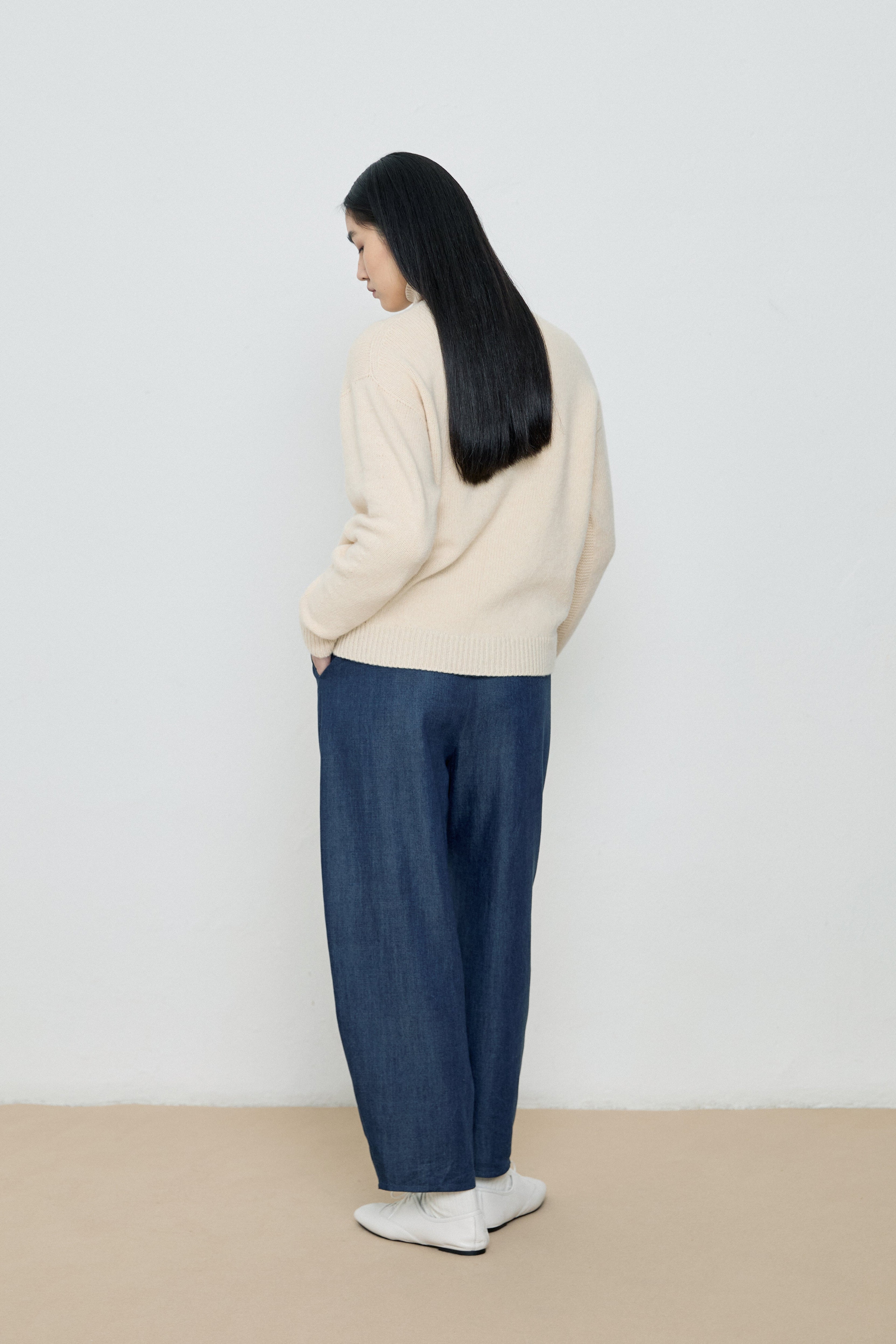 Person wearing a beige sweater and blue pants against a white background