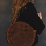 Person carrying a brown round bag against a dark background