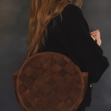 Person carrying a brown round bag against a dark background