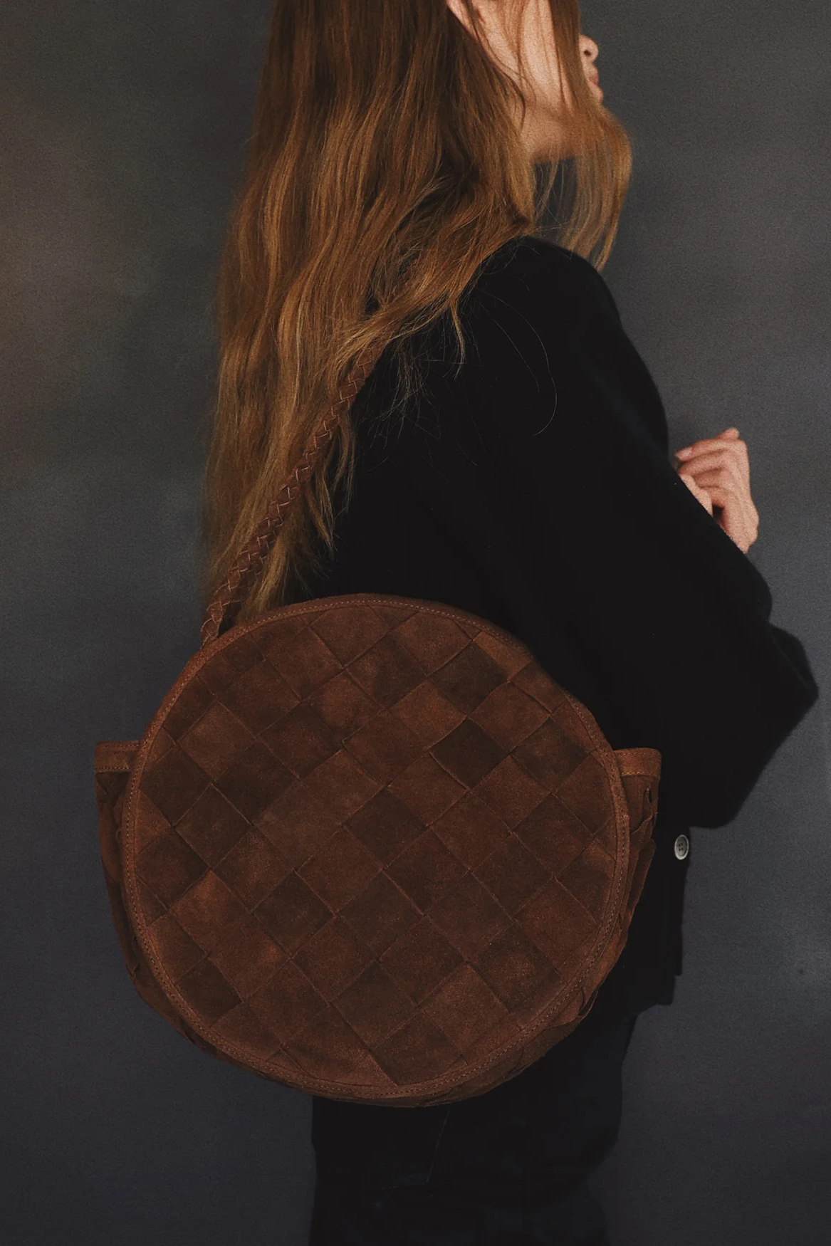Person carrying a brown round bag against a dark background