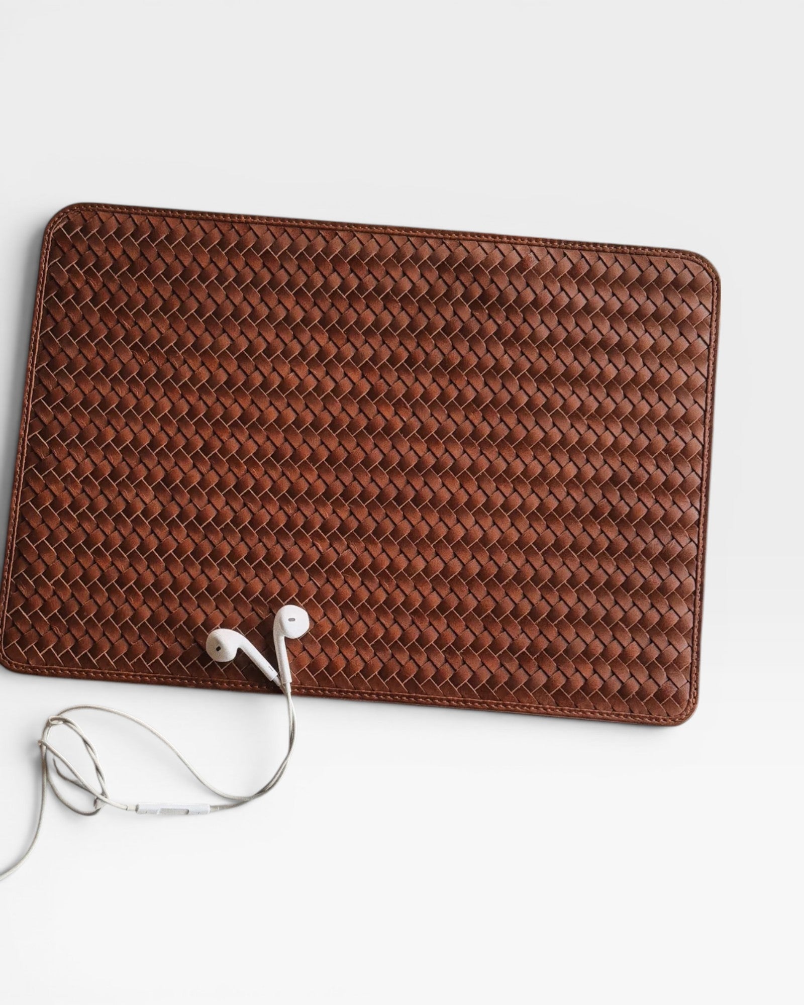 Brown woven leather wallet with earphones on a light gray surface