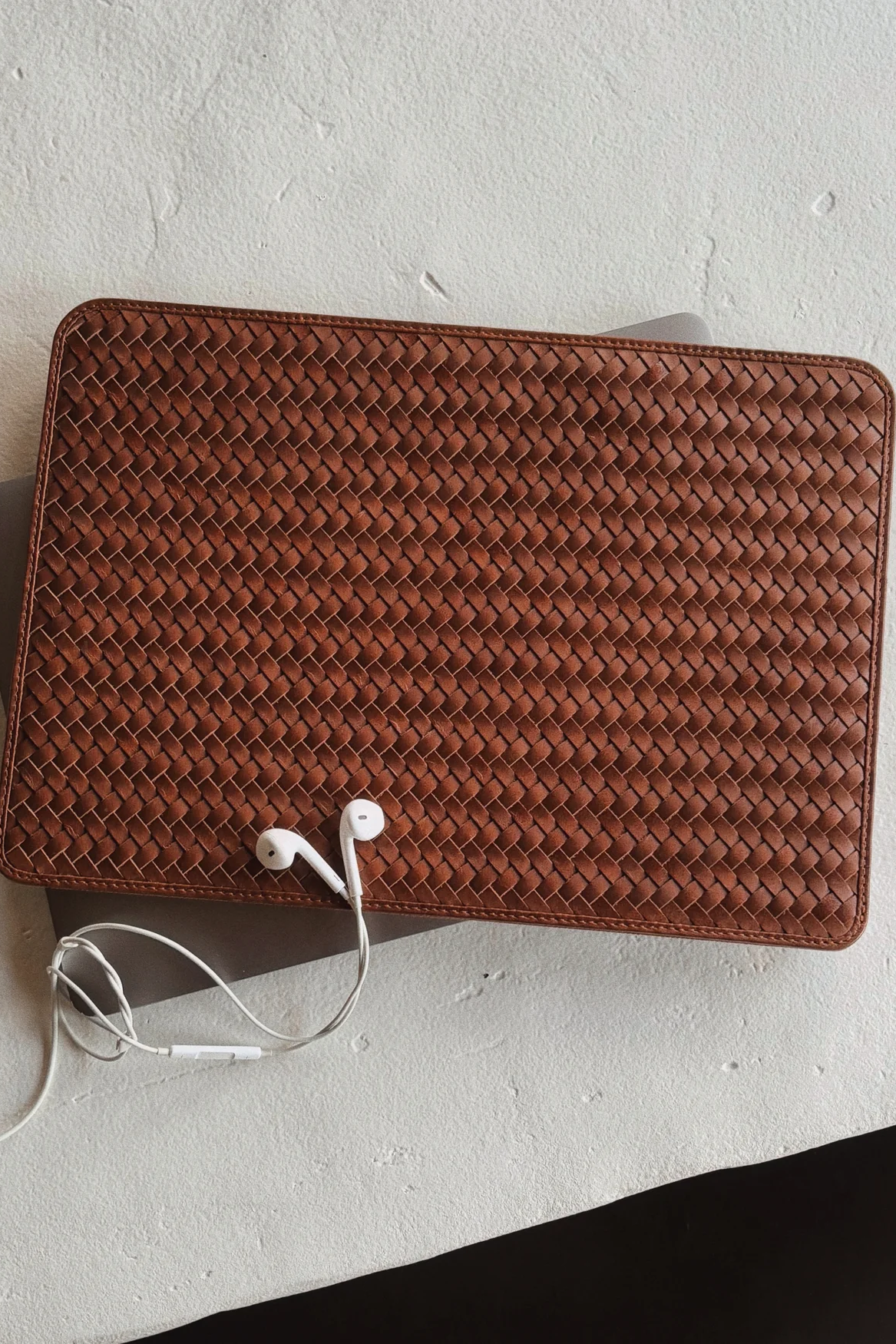 Brown woven leather wallet with earphones on a light gray surface