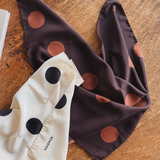 Two polka dot scarves, one white with black dots and the other brown with lighter brown dots, on a wooden surface.