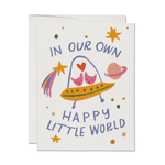 Greeting card with colorful illustration of a baby in a stroller, planet, and rainbow with text 'In our own happy little world' on a white background.